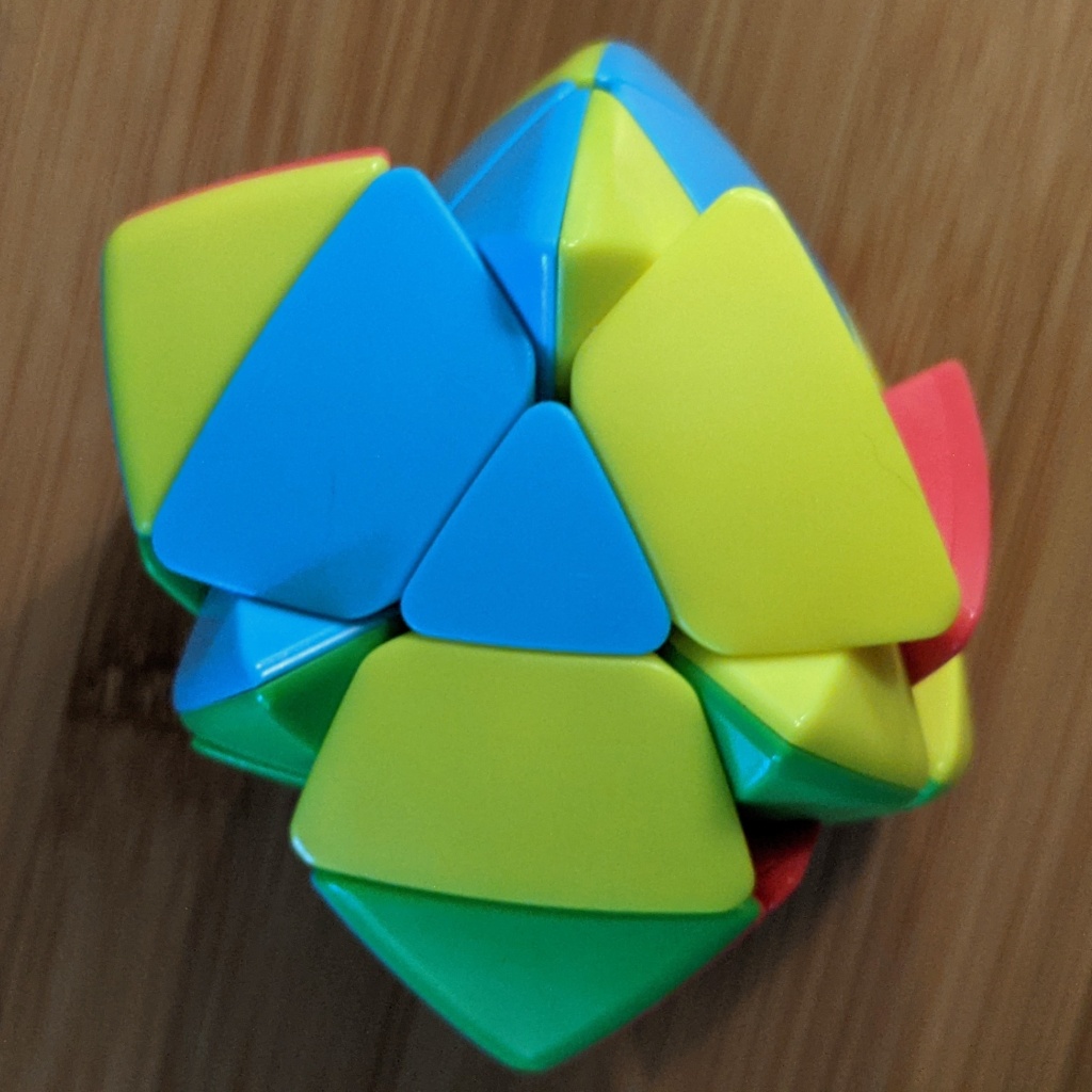 Photo of an unsolved twisty puzzle showing three center-type pieces, blue/green, green/yellow, and yellow/blue, forming a triangle and pointing up in the same direction